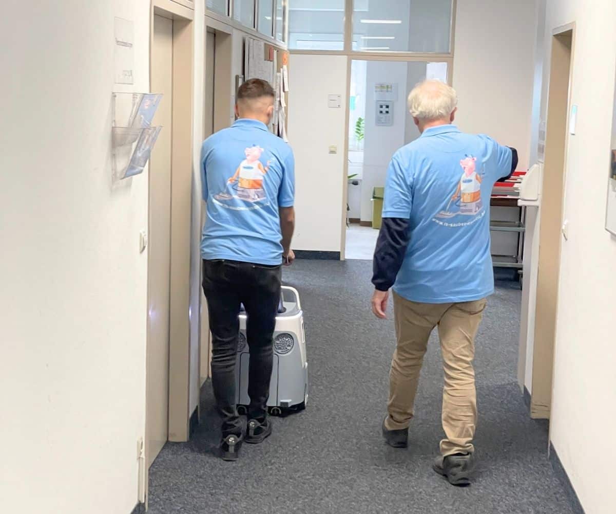 Zwei Reinigungskräfte von TS-SAUBER in blauen Schulungsshirts bei der praktischen Anwendung eines Reinigungsroboters im Büroflur – Teil einer Schulung zur Digitalisierung und effizienten Reinigungstechnik.